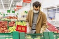 A young man in a medical mask is choosing fruits in a large supermarket. Precautions during the coronavirus pandemic. Healthy