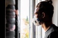 Young man in a medical mask, looks out the window and is reflected in the glass Royalty Free Stock Photo