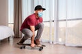 A young man in a medical mask poses, sitting on a longboard. Indoor. Home. The concept of quarantine and activity at home Royalty Free Stock Photo