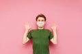 Young man in a medical mask stands on a pink background, looks at the camera and shows his palms. Frightened guy in a protective Royalty Free Stock Photo