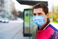 Young man in medical mask waiting for bus on empty bus stop