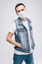 Young man in medical mask and wearing denim clothes, standing over white isolated background. Royalty Free Stock Photo