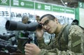 Young man in military uniform looking through portable monocular telescope, gun shop