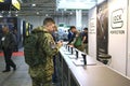 Young man in military uniform standing in front of the stand with pistols Glock presented and looking at them