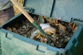 A young man is mixin the organic waste throwed to the outdoor compost bin.The compost bin is placed in a home garden to recycle