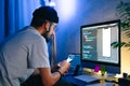 Young man mobile developer writes program code on a computer and check app in smartphone, programmer work in home office