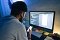 Young man mobile developer writes program code on a computer and check app in smartphone, programmer work in home office Royalty Free Stock Photo