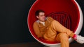 Young man with mobile phone sitting in ball chair on black background. Male browsing smartphone and resting in modern