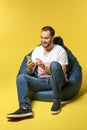 Young man with mobile phone sitting on beanbag chair against color background Royalty Free Stock Photo