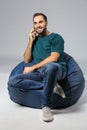 Young man with mobile phone sitting on beanbag chair against grey background Royalty Free Stock Photo