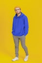 Young man model in casual wear, glasses posing looking at camera on yellow background with hands in pockets. Stylish Royalty Free Stock Photo