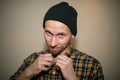 Young man, model of fashion, wearing a plaid shirt with a biege blind behind him. Guy in black hat with beard in casual Royalty Free Stock Photo