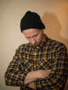 Young man, model of fashion, wearing a plaid shirt with a biege blind behind him. Guy in black hat with beard in casual Royalty Free Stock Photo