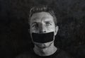 Young man with mouth and lips sealed covered with adhesive tape in censorship coerced freedom of speech and forced silence and sec Royalty Free Stock Photo