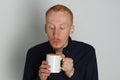 A young man with a mug of tea or coffee. He pleased. White background. Redhead male with white mug. Royalty Free Stock Photo