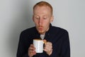 A young man with a mug of tea or coffee. He pleased. White background. Redhead male with white mug. Royalty Free Stock Photo