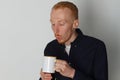 A young man with a mug of tea or coffee. He pleased. White background. Redhead male with white mug. Royalty Free Stock Photo