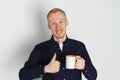 A young man with a mug of tea or coffee. He pleased. White background. Redhead male with white mug. Royalty Free Stock Photo