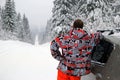 Young man near to a car on the winter road with snow covered firs. Royalty Free Stock Photo