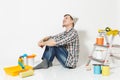 Young man in newspaper hat sitting on floor with instruments for renovation apartment room isolated on white background Royalty Free Stock Photo