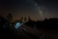 Young man observes starry sky through a telescope. Mountains, surrouded by pine tree forest in the background night landscape with Royalty Free Stock Photo