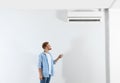 Young man operating air conditioner with remote  indoors. Space for text Royalty Free Stock Photo