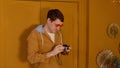 Young man in orange glasses with old photo camera stands against background of brown doors in room. Stylish male