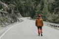 A young man with an outdoor dress and a road passing through the pine forest