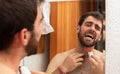 young man in pain grooming shaving and trim the beard with electric razor cutting mustache on the mirror feeling irritation Royalty Free Stock Photo