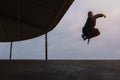 Young man in pants and hoodie jumping on factory ramp. Mid air parkour pose in with overcast sky Royalty Free Stock Photo