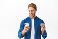 Young man paying with smartphone app, smiling while looking at mobile phone screen, holding credit card. Online shopping