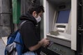 The young man performs his transactions from the bank atm using his protective mask
