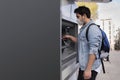 The young man performs his transactions from the bank atm using his protective mask