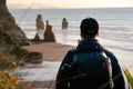 Young man with photographer backpack looking at scenic view of limestone formations by the beach