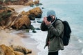 Young man photographer traveler with backpack taking pictures on sea and rocks background. Place for text or advertising Royalty Free Stock Photo