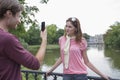 Young man photographing woman through cell phone at lakeside