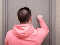 A young man in a pink hoodie knocks on a wooden door. Guest. Rear view bangs knocking on the door with his hand Royalty Free Stock Photo