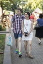 A young man in a plaid shirt and a girl in a white dress embracing each other are walking down the street