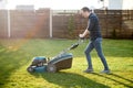 Young man in a plaid shirt and jeans mows lawn Royalty Free Stock Photo