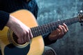 Young man playing an acoustic guitar on the background of a concrete wall