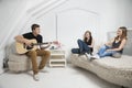 Young man playing guitar with female friends sitting on sofa Royalty Free Stock Photo