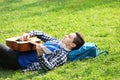 Young man playing guitar while lying on green grass in park Royalty Free Stock Photo