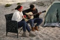 Young man playing guitar to his beloved girlfriend near camping tent on beach Royalty Free Stock Photo