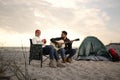 Young man playing guitar to his beloved girlfriend near camping tent on beach Royalty Free Stock Photo