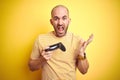 Young man playing video games using joystick gamepad over isolated yellow background very happy and excited, winner expression Royalty Free Stock Photo