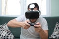 Young man playing video games with virtual reality headset and a gamepad sitting on sofa Royalty Free Stock Photo