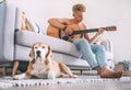 Young man plays on guitar sitting on the sofa at home and beagle Royalty Free Stock Photo