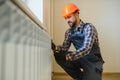 young man plumber checking radiator while installing heating system in apartment