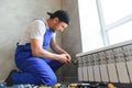 young man plumber checking radiator while installing heating system in apartment