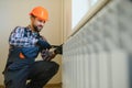 young man plumber checking radiator while installing heating system in apartment